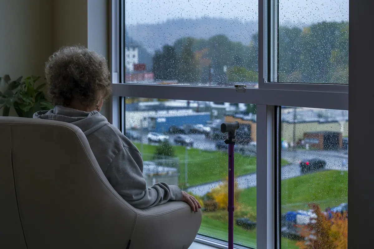 Senhora sentada na poltrona olha pela janela em um dia de chuva.