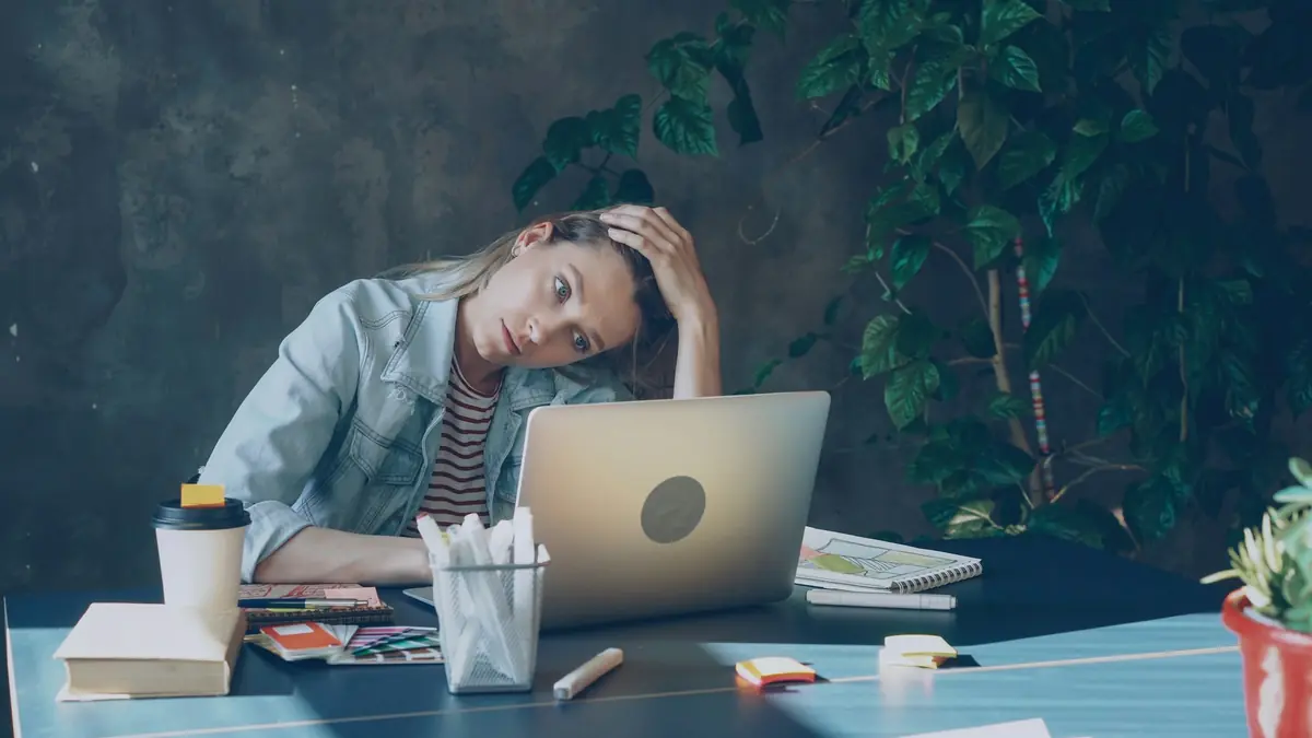 Mulher exausta apoia a cabeça na mão diante do notebook.