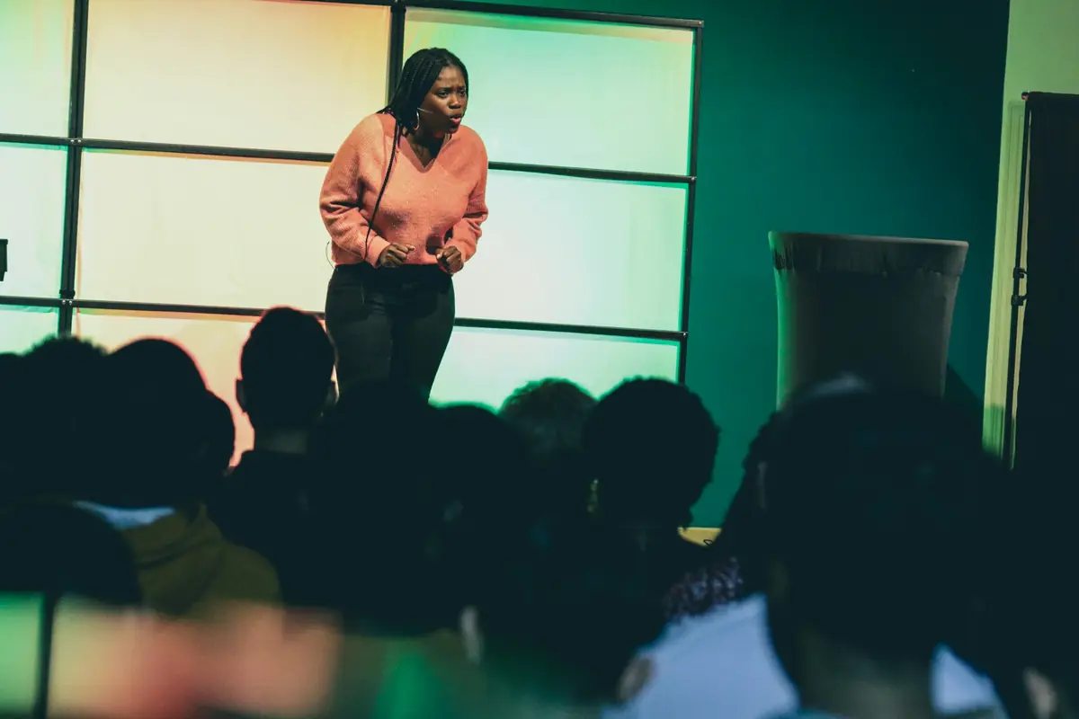 Mulher em um palco diante da plateia, observada por todos.