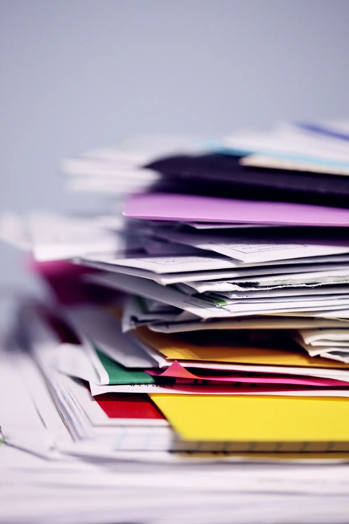 Pilha desordenada de papéis e envelopes coloridos.